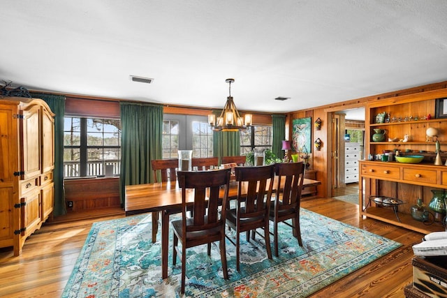 dining space with wooden walls, a healthy amount of sunlight, light hardwood / wood-style floors, and a notable chandelier