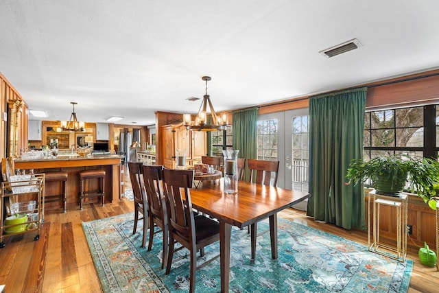 dining room with light hardwood / wood-style floors, french doors, and an inviting chandelier