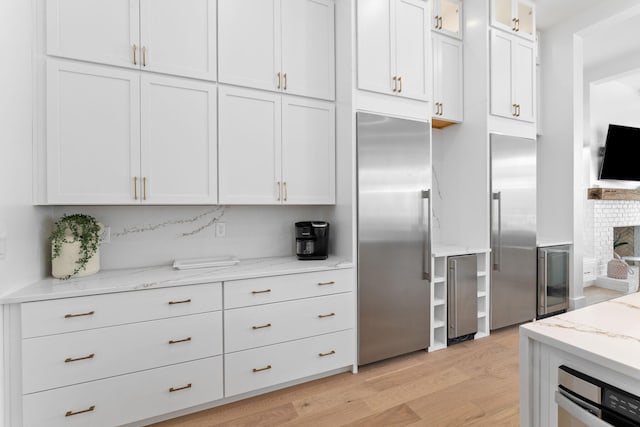 kitchen with high quality fridge, light stone countertops, light hardwood / wood-style floors, and white cabinets