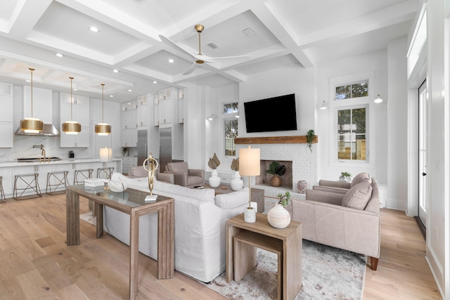 living room featuring beamed ceiling, light hardwood / wood-style flooring, sink, coffered ceiling, and ceiling fan