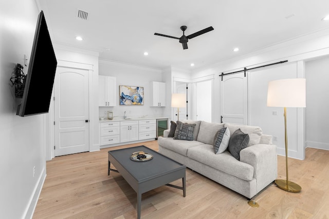 living room with a barn door, ceiling fan, crown molding, sink, and light wood-type flooring