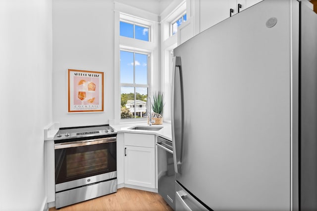 kitchen with sink, appliances with stainless steel finishes, light wood-type flooring, and white cabinetry