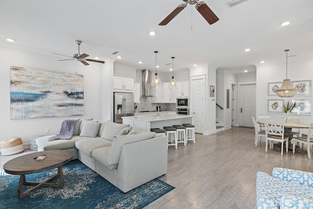 living room with ornamental molding, sink, light hardwood / wood-style floors, and ceiling fan with notable chandelier