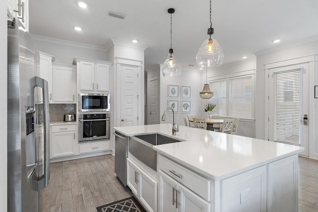 kitchen featuring appliances with stainless steel finishes, white cabinets, tasteful backsplash, decorative light fixtures, and a kitchen island with sink