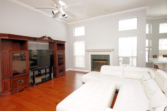 living room featuring hardwood / wood-style floors, a high ceiling, a high end fireplace, ceiling fan, and ornamental molding