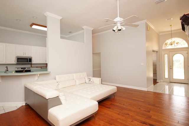 living room featuring a towering ceiling, light wood-type flooring, ceiling fan with notable chandelier, and ornamental molding