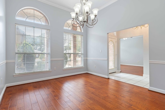 unfurnished dining area featuring a high ceiling, crown molding, a notable chandelier, and light hardwood / wood-style flooring