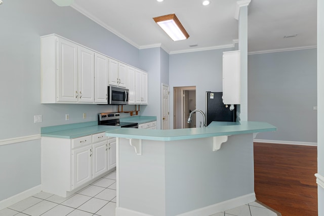 kitchen featuring a breakfast bar, white cabinetry, light tile patterned floors, ornamental molding, and stainless steel appliances