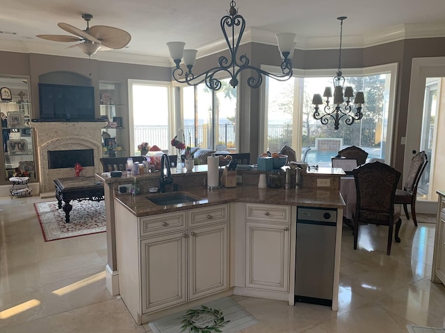 kitchen featuring dark stone counters, ceiling fan with notable chandelier, a kitchen island with sink, sink, and hanging light fixtures