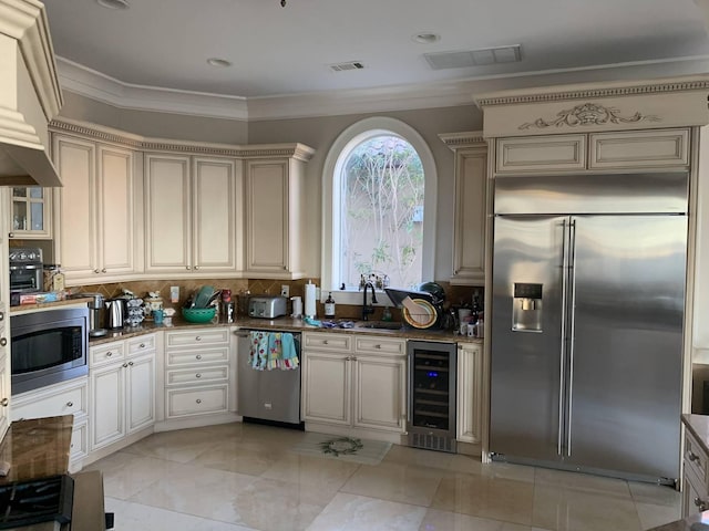 kitchen featuring backsplash, beverage cooler, sink, built in appliances, and cream cabinetry