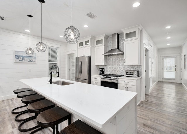 kitchen featuring light hardwood / wood-style floors, appliances with stainless steel finishes, wall chimney range hood, and an island with sink