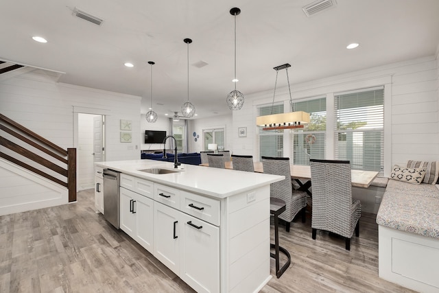 kitchen featuring a kitchen bar, light hardwood / wood-style floors, white cabinetry, hanging light fixtures, and an island with sink