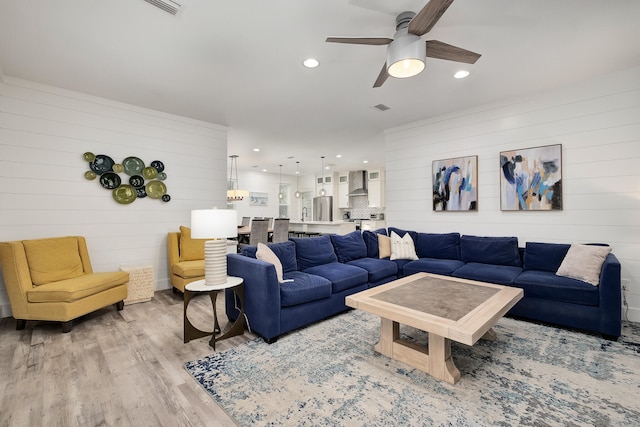 living room with light hardwood / wood-style floors, ceiling fan, and wooden walls