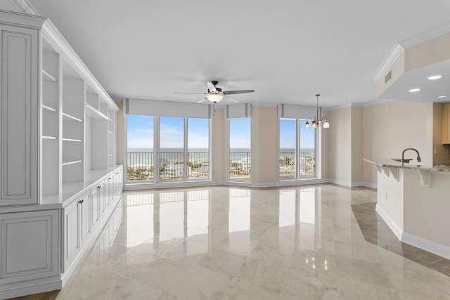 unfurnished living room with ceiling fan with notable chandelier, a wealth of natural light, ornamental molding, and sink