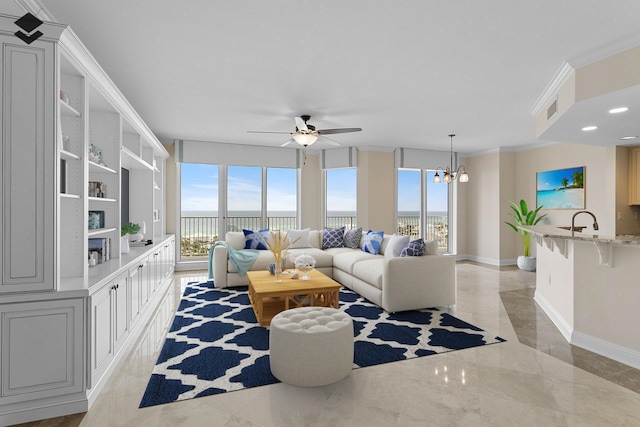 living room featuring ceiling fan with notable chandelier, a healthy amount of sunlight, ornamental molding, and sink