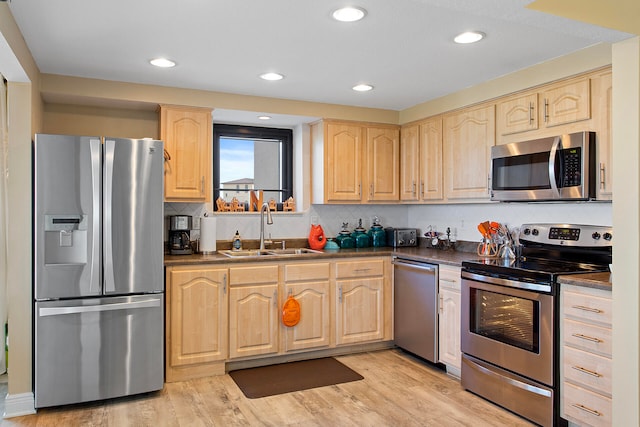 kitchen with light brown cabinets, a sink, appliances with stainless steel finishes, light wood finished floors, and dark countertops