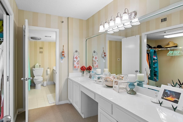 bathroom featuring toilet, a textured ceiling, vanity, baseboards, and wallpapered walls