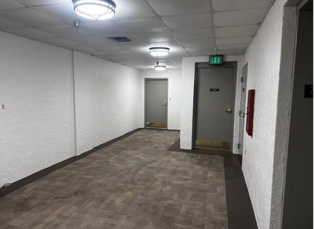 empty room with visible vents, dark carpet, a drop ceiling, and a textured wall