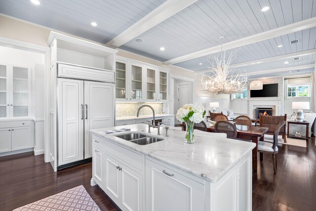 kitchen featuring beam ceiling, an island with sink, white cabinetry, sink, and pendant lighting