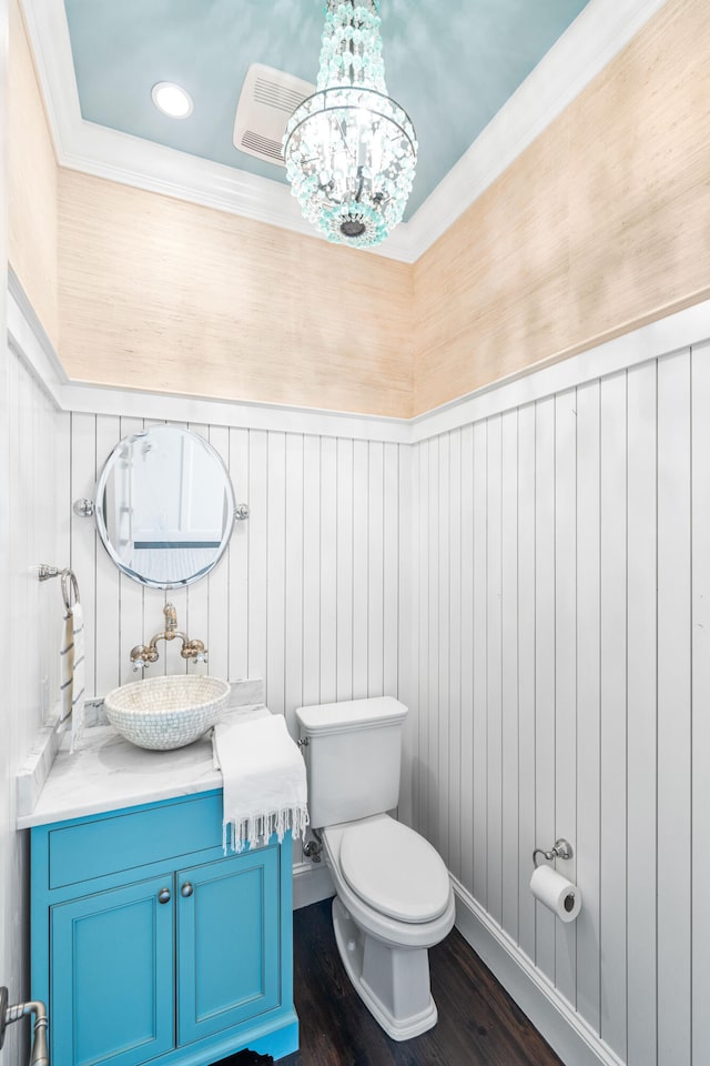 bathroom with wood-type flooring, ornamental molding, an inviting chandelier, oversized vanity, and toilet