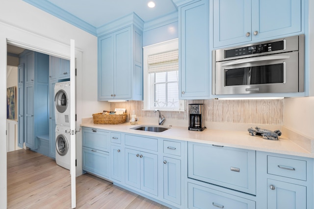 kitchen with stacked washer / dryer, sink, backsplash, crown molding, and light hardwood / wood-style flooring