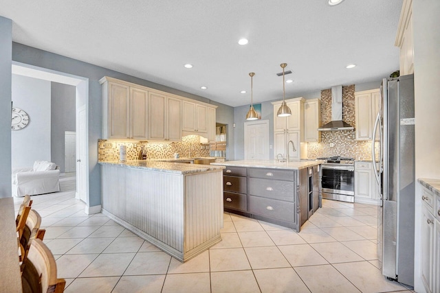 kitchen with light stone countertops, backsplash, stainless steel appliances, wall chimney exhaust hood, and a kitchen island with sink