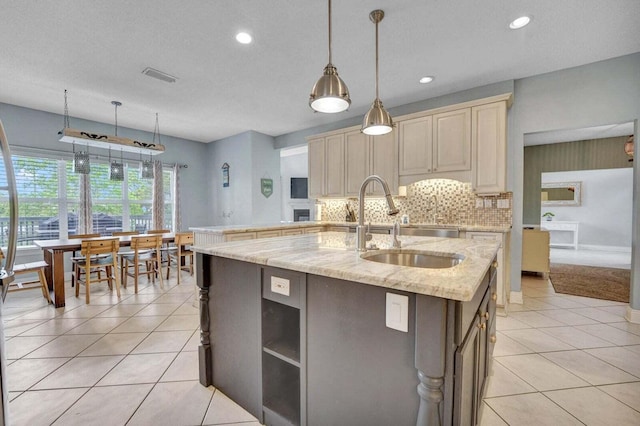 kitchen featuring light tile floors, sink, backsplash, hanging light fixtures, and an island with sink