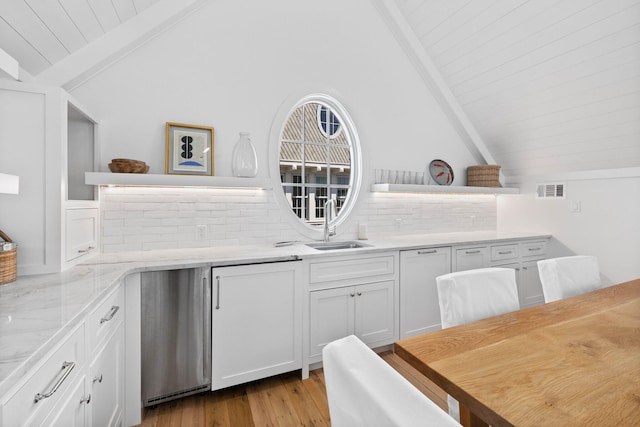 kitchen featuring light stone countertops, backsplash, light hardwood / wood-style floors, beamed ceiling, and white cabinets