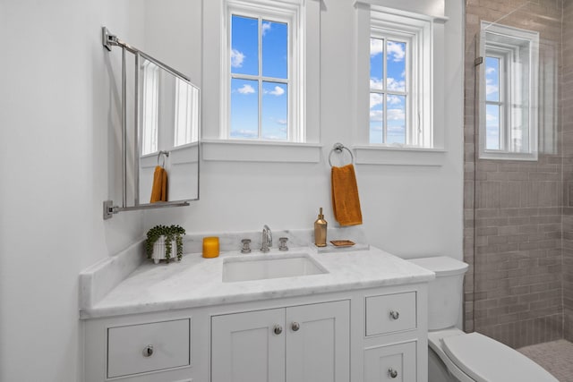 bathroom featuring tiled shower, plenty of natural light, toilet, and large vanity