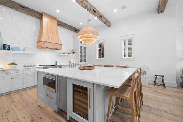 kitchen with wine cooler, light wood-type flooring, backsplash, custom range hood, and a kitchen island