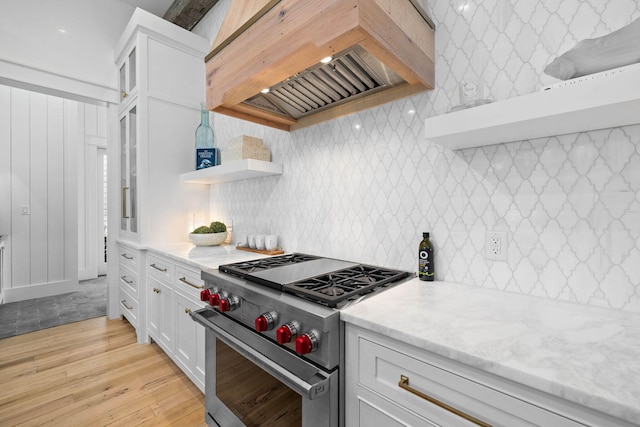 kitchen featuring premium stove, custom exhaust hood, light stone counters, white cabinets, and light wood-type flooring