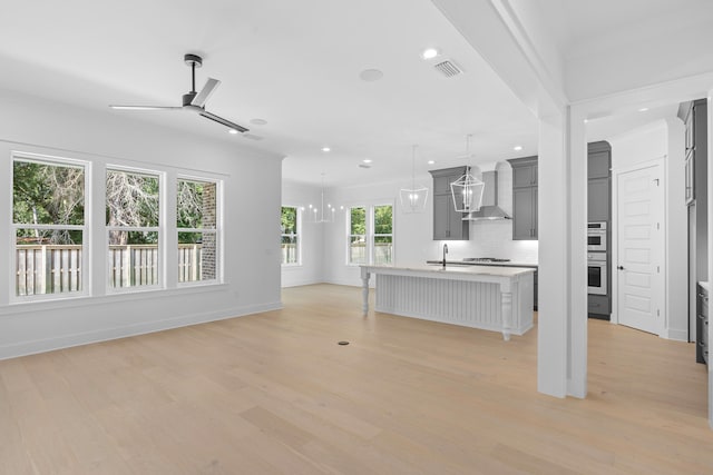 kitchen with a wealth of natural light, wall chimney range hood, a kitchen island with sink, and light wood-type flooring