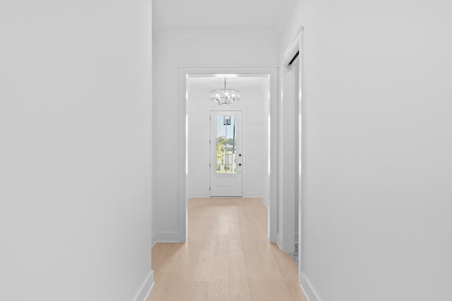 hall featuring ornamental molding, light wood-type flooring, and a chandelier