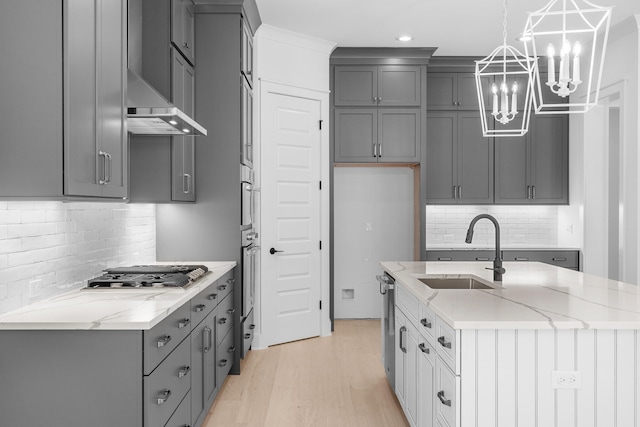 kitchen with sink, light stone countertops, light wood-type flooring, appliances with stainless steel finishes, and decorative light fixtures