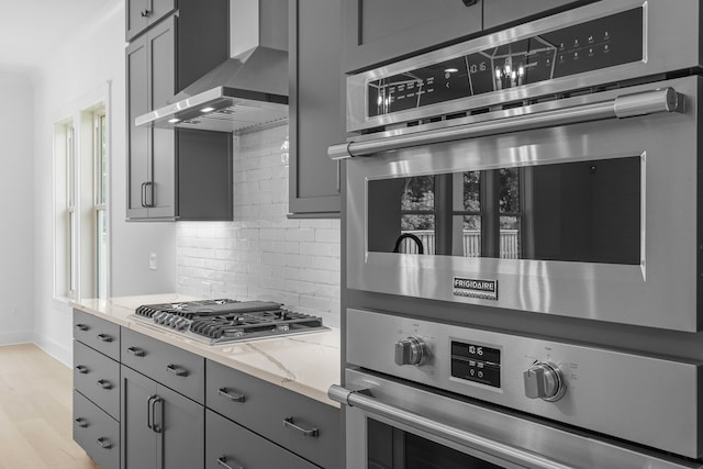 kitchen with light hardwood / wood-style floors, stainless steel gas cooktop, light stone countertops, wall chimney range hood, and decorative backsplash