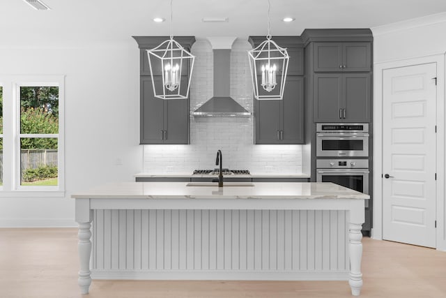 kitchen with light stone countertops, wall chimney range hood, and a kitchen island with sink