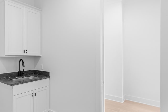 bar featuring white cabinets, dark stone countertops, sink, and light hardwood / wood-style flooring