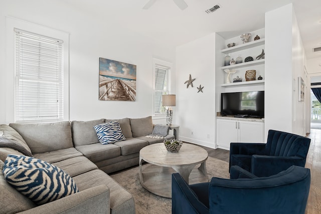 living room featuring built in shelves, ceiling fan, and wood-type flooring