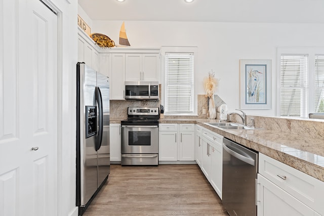 kitchen featuring sink, backsplash, appliances with stainless steel finishes, white cabinets, and light wood-type flooring