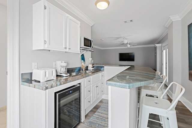 kitchen with wine cooler, white cabinetry, crown molding, and hardwood / wood-style floors