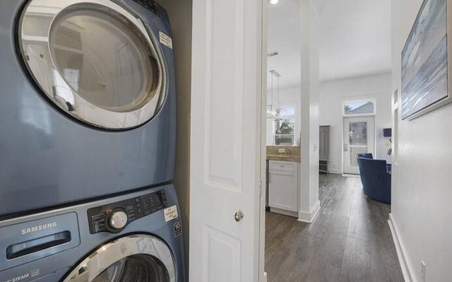 laundry area featuring dark wood-type flooring, stacked washer / drying machine, and a notable chandelier