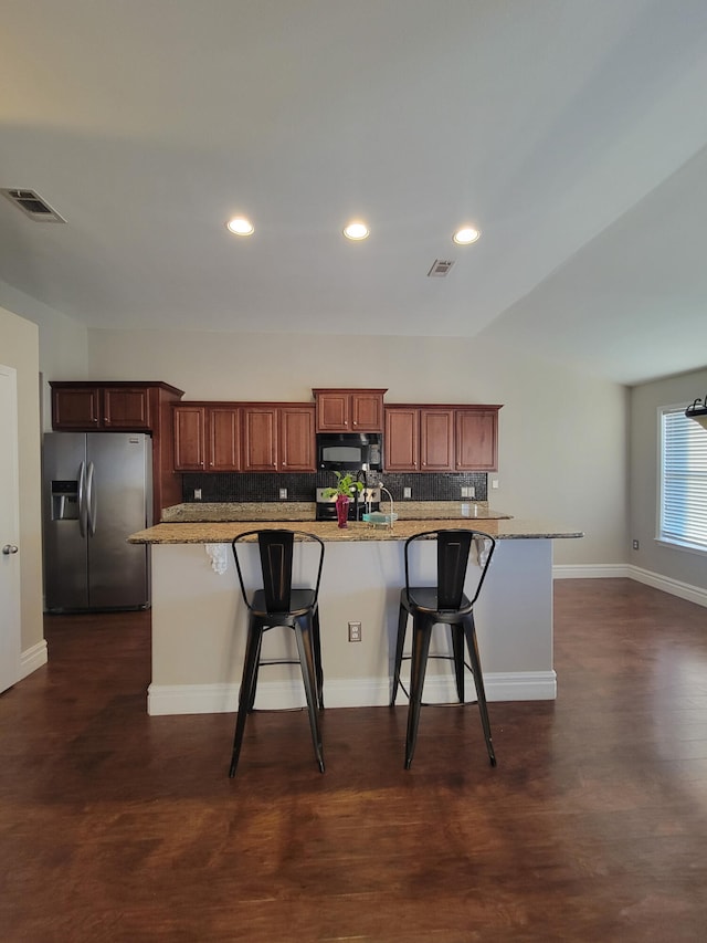 kitchen with a breakfast bar, sink, decorative backsplash, light stone countertops, and stainless steel fridge