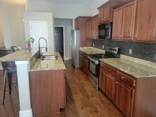 kitchen with appliances with stainless steel finishes, sink, a kitchen island with sink, dark wood-type flooring, and a breakfast bar