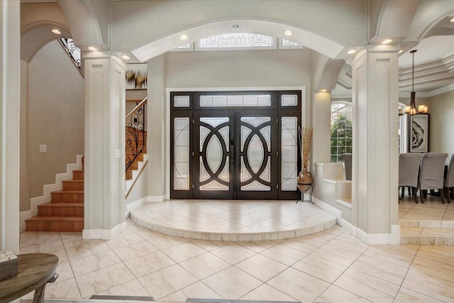 tiled foyer entrance featuring decorative columns, ornamental molding, and a notable chandelier