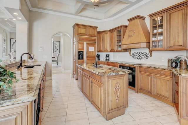 kitchen with black appliances, sink, a kitchen island with sink, light stone countertops, and custom range hood