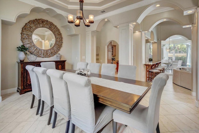 dining area with a tray ceiling, an inviting chandelier, ornamental molding, and ornate columns