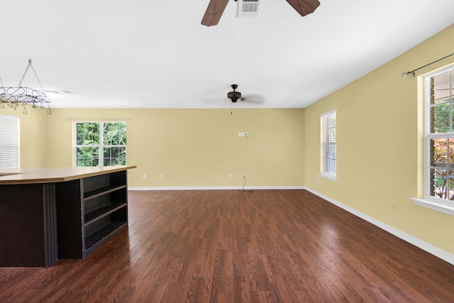 unfurnished living room featuring baseboards, visible vents, dark wood-type flooring, and a wealth of natural light