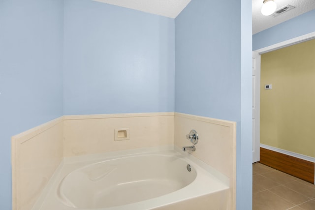 full bath featuring a textured ceiling, tile patterned flooring, a garden tub, visible vents, and baseboards