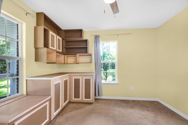 interior space with light carpet, light countertops, a ceiling fan, and baseboards