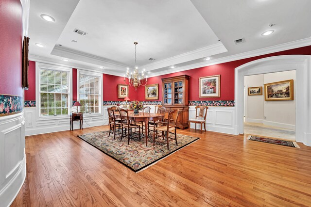 dining space featuring ornamental molding, light hardwood / wood-style flooring, a notable chandelier, and a raised ceiling